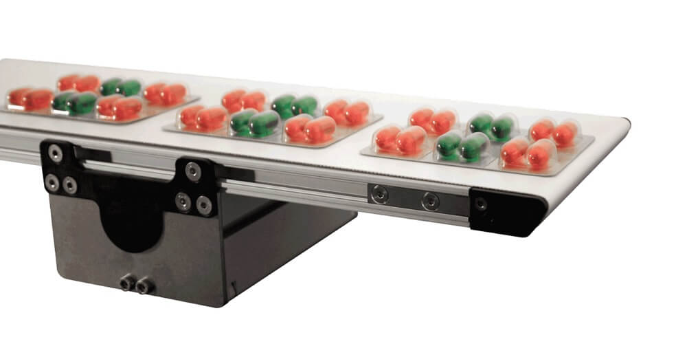 A Dorner 1100 series mini conveyor transporting pill packs or orange and green pills.